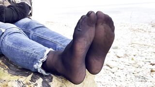 Feet tease in black and grey nylon socks wiggling toes at the seashore