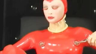 Sexy girl encased in red rubber catsuit loves medical games with mouth spreader and nipple clamps